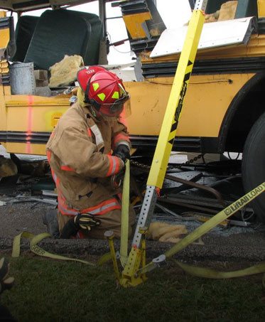 A firefighter setting a hydraulic strut against a wrecked school bus